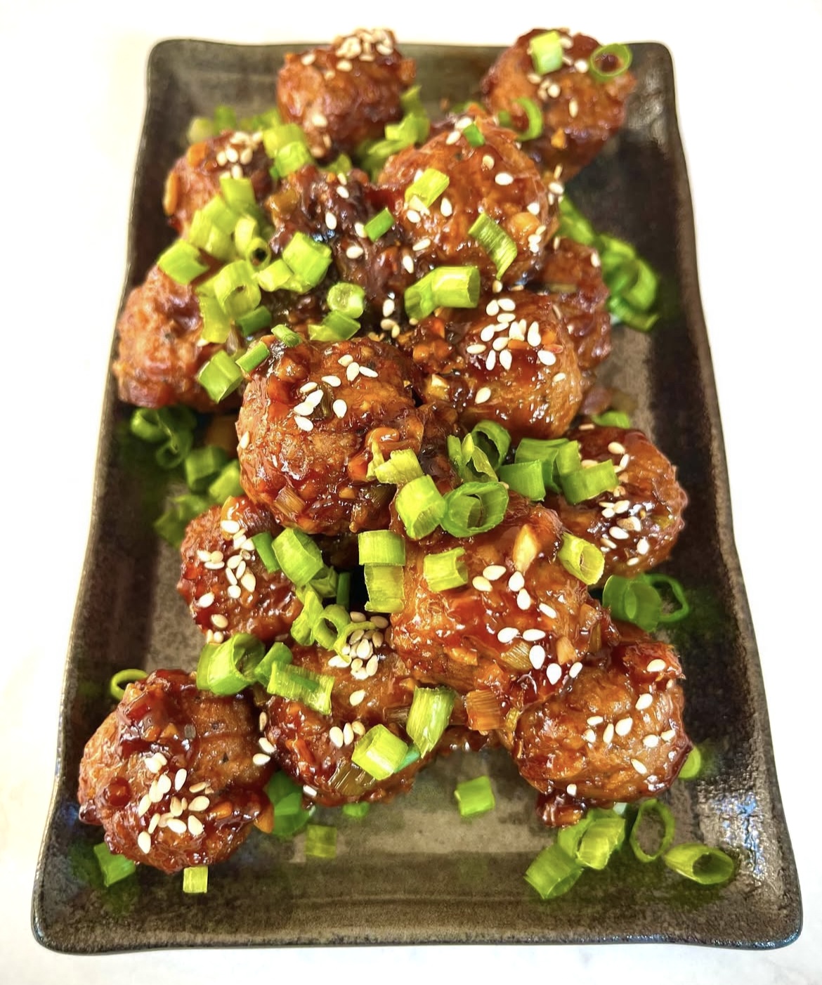 asian bbq roasted cauliflower with green onions on a dark plate