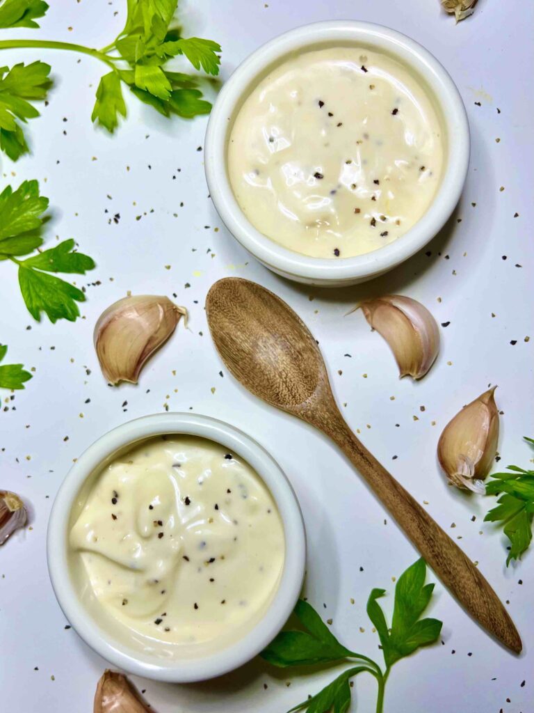 lemon garlic aioli in two cups with spoon and garnishes seen from top