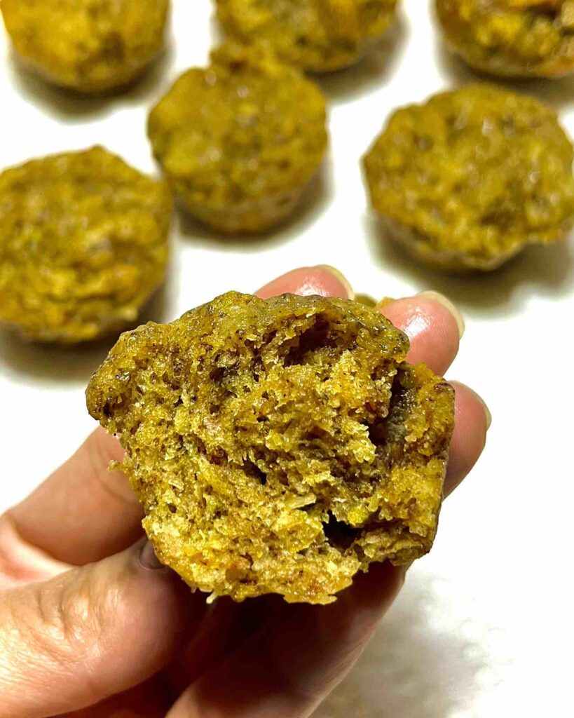 close-up of hand holding a mini orange coconut muffin with a bite missing