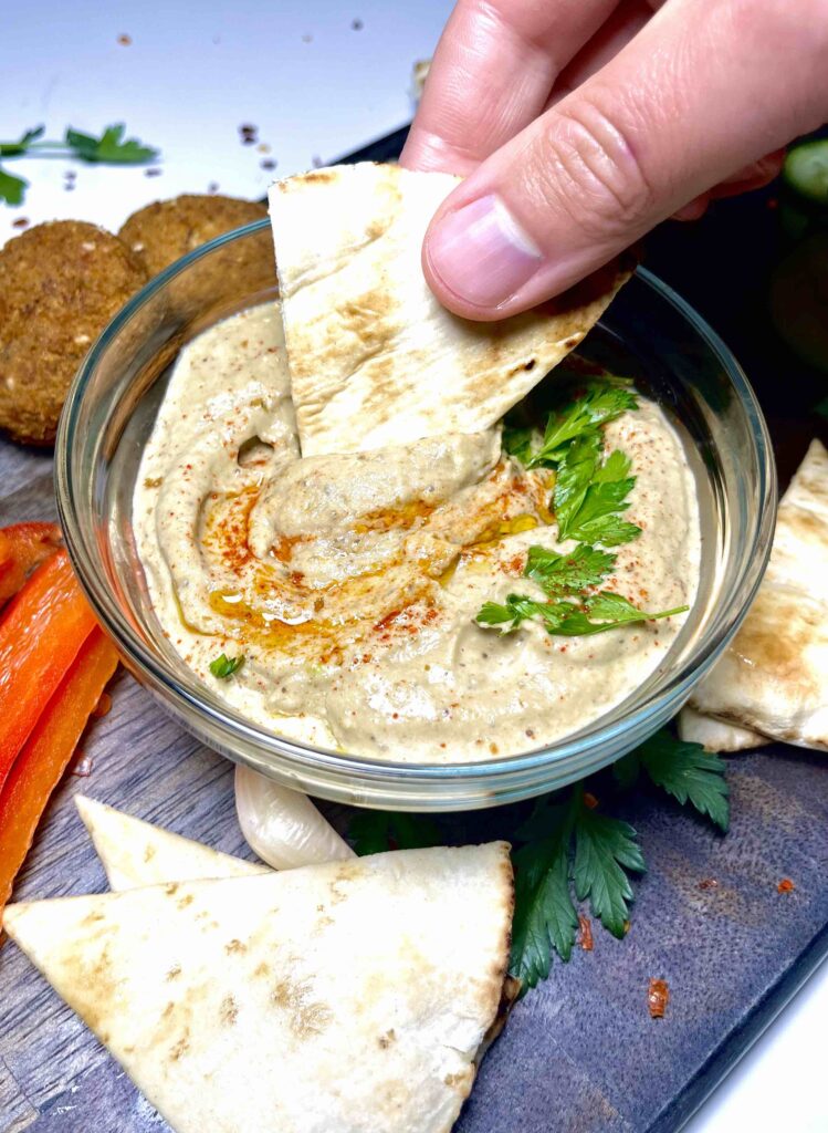 hand dipping pita bread into baba ganoush on platter