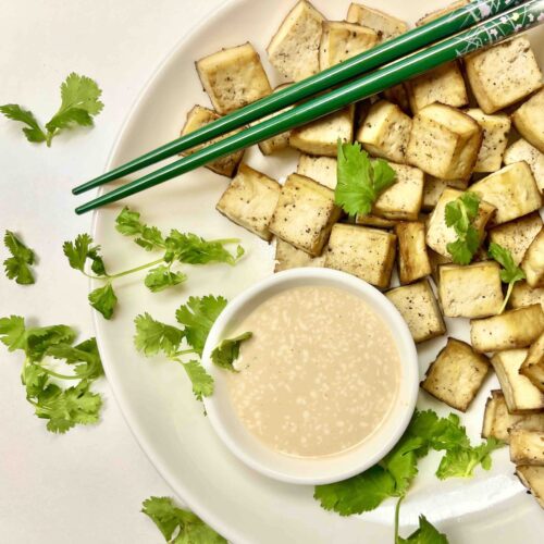 baked tofu cubes on plate with sauce and chopsticks