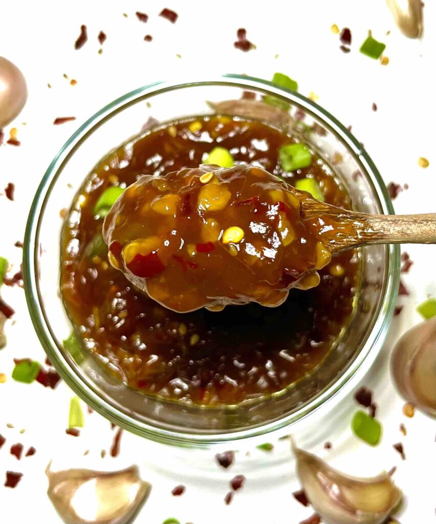 close-up of spoon lifting chinese garlic sauce with bowl in background