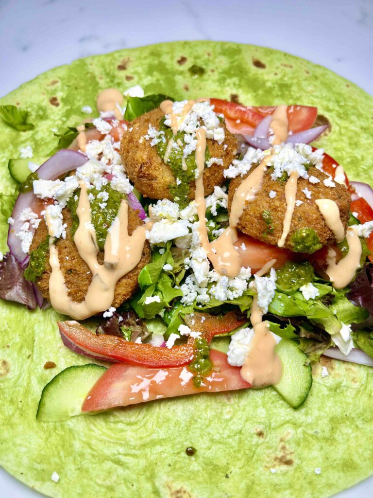 assembling a falafel wrap with ingredients in center