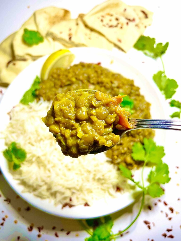 spoonful of spiced brown lentils in close-up with plate of lentils and rice in background
