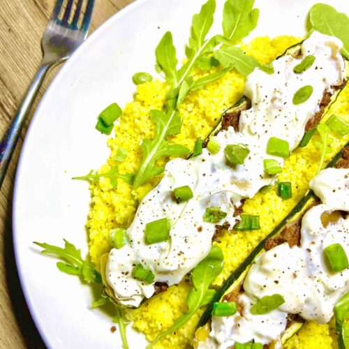 stuffed zucchini boats on bed of couscous on plate with fork