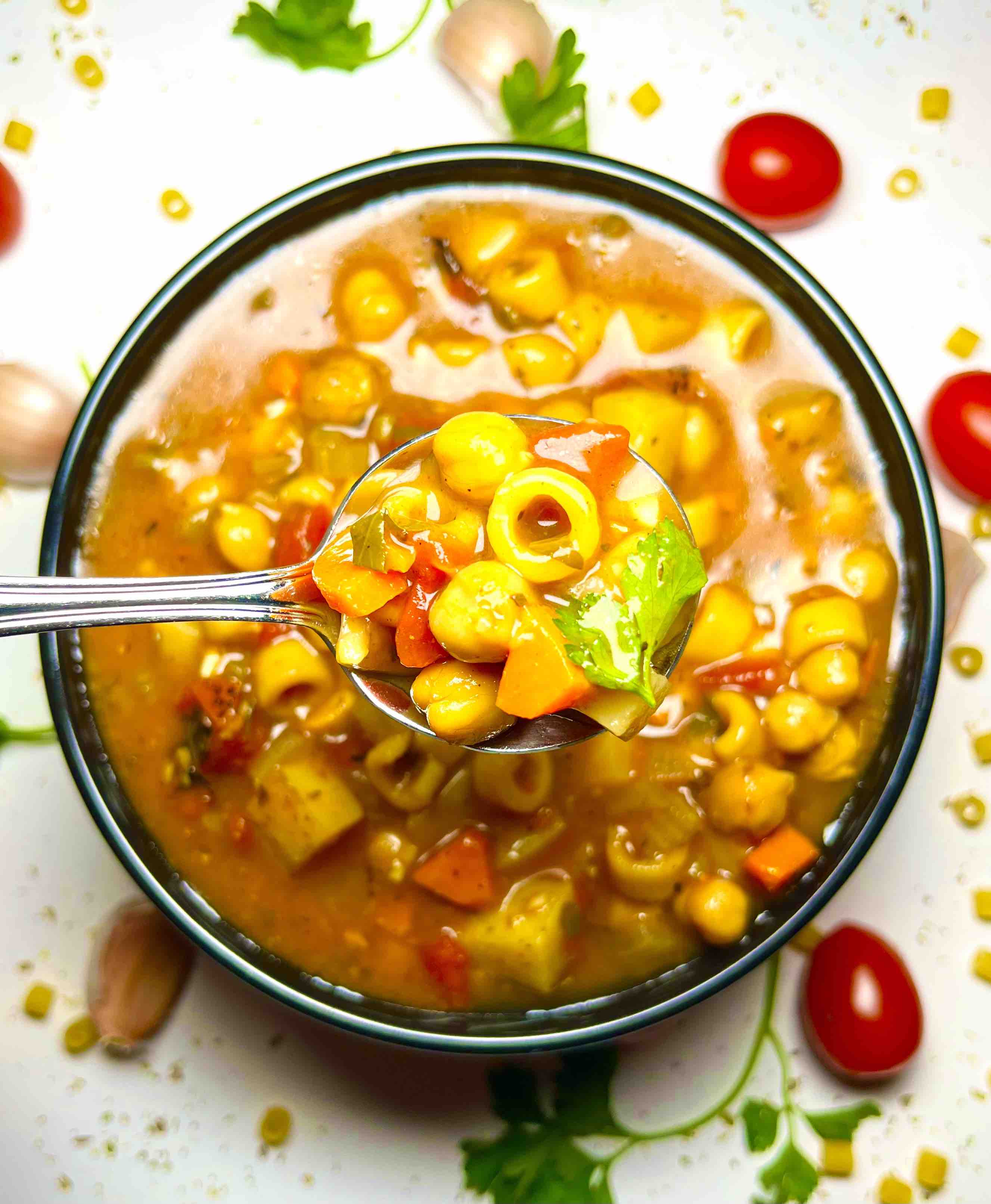 vegan minestrone soup in black bowl with spoon surrounded by garnishes