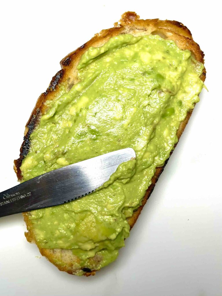 avocado mash being spread on slice of toast