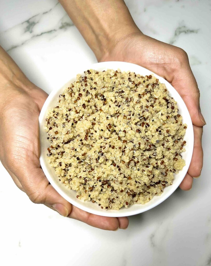 bowl of cooked quinoa being held by two hands seen from above
