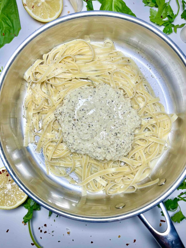 cooked fettuccine noodles and alfredo sauce unmixed in a stainless steel pan with garnishes around edges