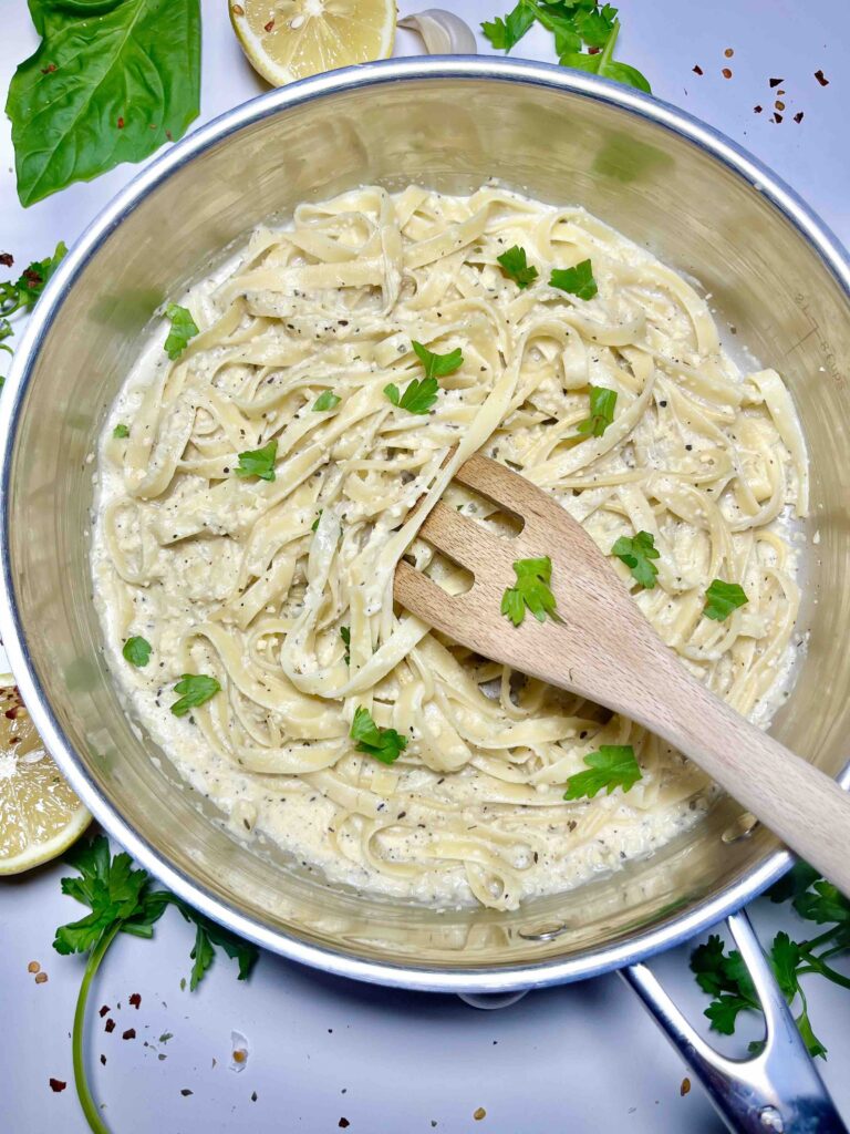 fettuccine alfredo pasta mixed with wooden spoon in stainless steel pan
