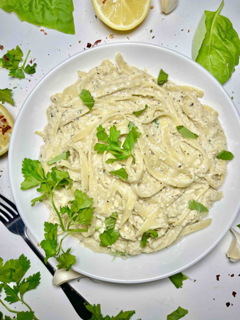 vegan fettuccine pasta on plate surrounded by garnishes and fork