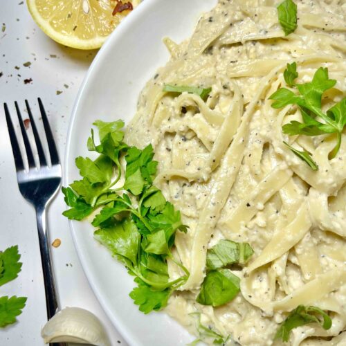 vegan fettuccine alfredo pasta on plate seen from above with fork and lemon wedge