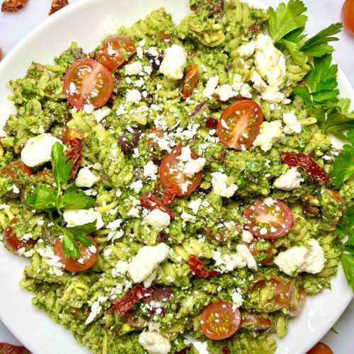 parsley pesto pasta salad on white plate surrounded by garnishes seen from above
