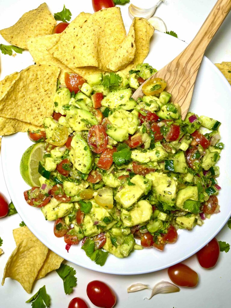 avocado salad on plate surrounded by corn chips and wooden spoon