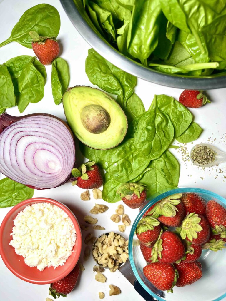 halved avocado, red onion, spinach, strawberries, and other ingredients seen from above