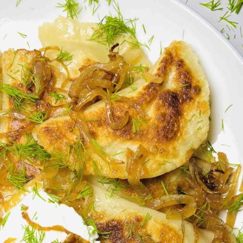 vegan pierogi spread on a plate seen from above with carmelized onions and sour cream
