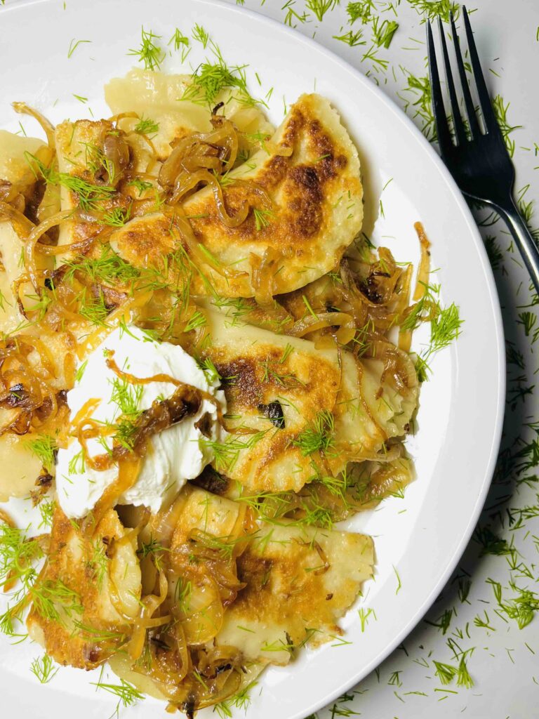 vegan pierogi on a plate with garnishes and a fork, seen from above